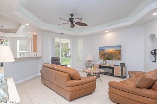 tiled living room featuring ceiling fan with notable chandelier, crown molding, and a tray ceiling