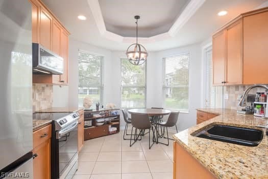 kitchen featuring appliances with stainless steel finishes, light brown cabinetry, sink, hanging light fixtures, and a tray ceiling