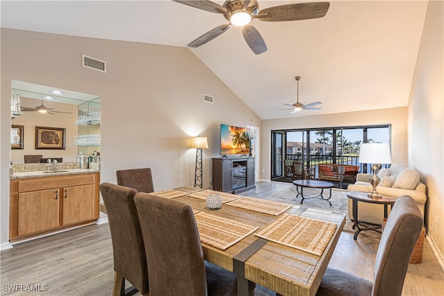 dining area with sink, high vaulted ceiling, light wood-type flooring, and ceiling fan