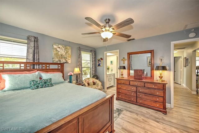 bedroom with ceiling fan, light hardwood / wood-style floors, ensuite bath, and multiple windows