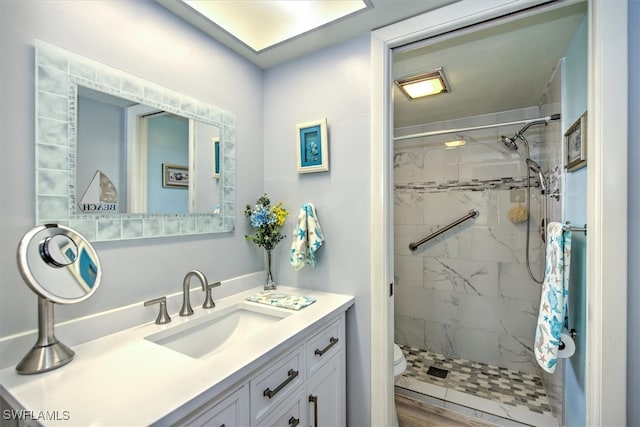 bathroom featuring a tile shower, hardwood / wood-style floors, vanity, and toilet