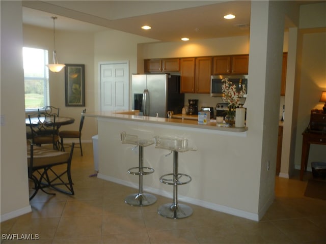 kitchen featuring a kitchen breakfast bar, stainless steel appliances, hanging light fixtures, and light tile patterned floors