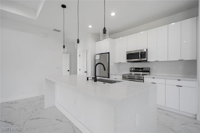 kitchen with an island with sink, stainless steel appliances, sink, decorative light fixtures, and white cabinets