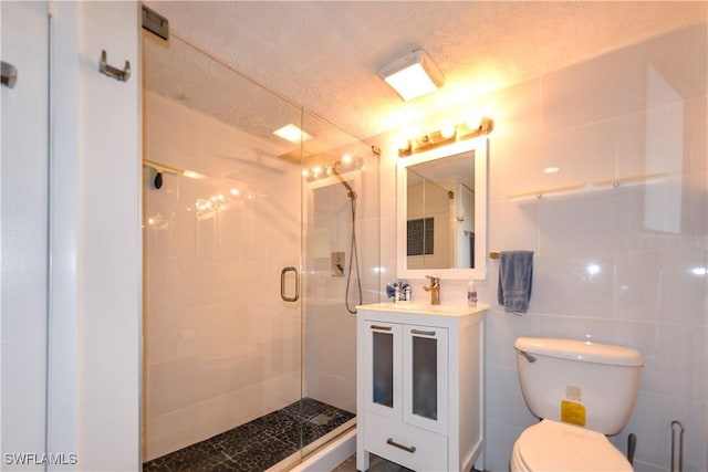 bathroom featuring vanity, a textured ceiling, a shower with door, tile walls, and toilet