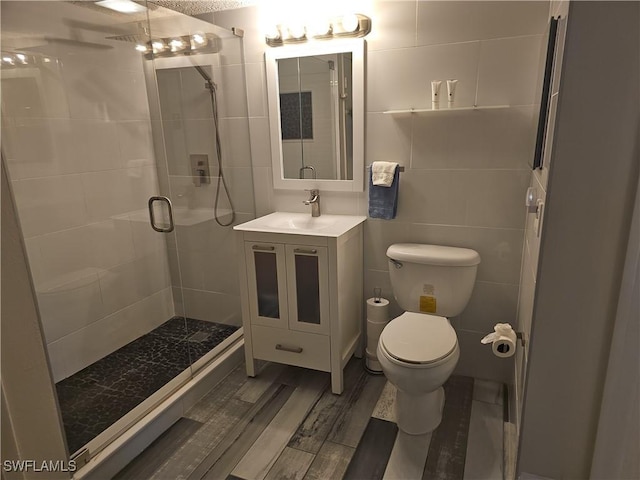 bathroom with walk in shower, vanity, tile walls, hardwood / wood-style floors, and toilet