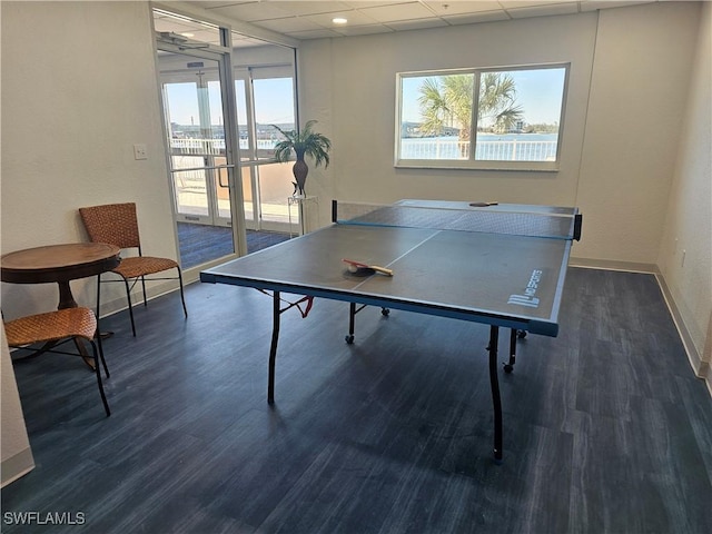 rec room with a drop ceiling, a healthy amount of sunlight, and dark wood-type flooring