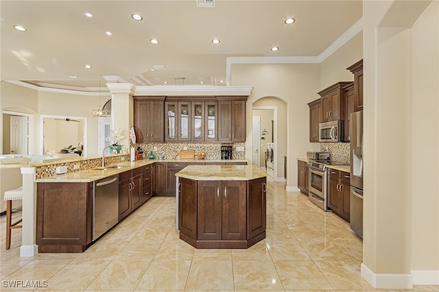 kitchen featuring kitchen peninsula, appliances with stainless steel finishes, washer and dryer, ornamental molding, and sink