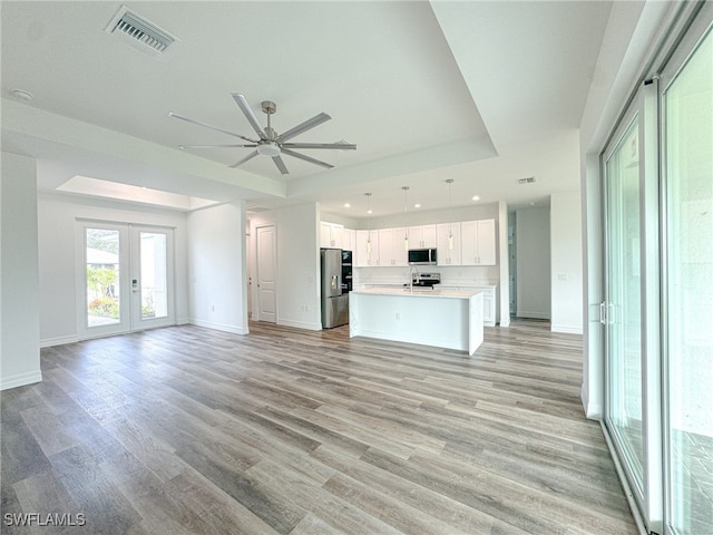 unfurnished living room featuring french doors, ceiling fan, a tray ceiling, and light wood-type flooring