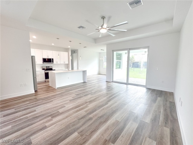 unfurnished living room featuring ceiling fan, a raised ceiling, and light hardwood / wood-style flooring