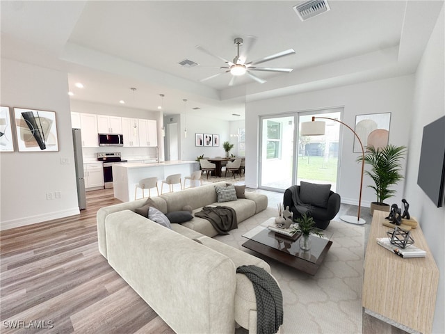 living room featuring light hardwood / wood-style floors, sink, a tray ceiling, and ceiling fan