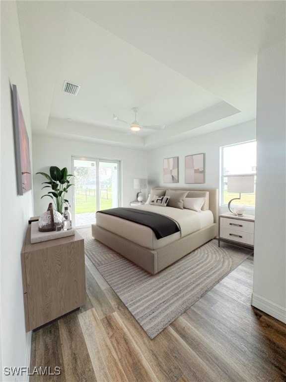 bedroom featuring ceiling fan, hardwood / wood-style flooring, access to outside, and a raised ceiling