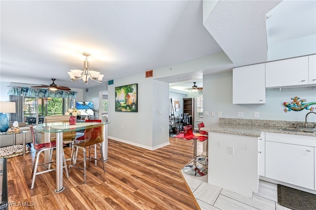 kitchen featuring ceiling fan with notable chandelier, light hardwood / wood-style floors, hanging light fixtures, sink, and white cabinetry