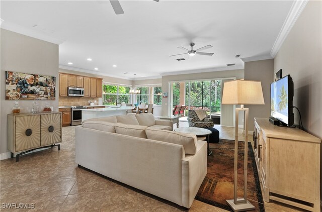 living room featuring a wealth of natural light, ornamental molding, ceiling fan with notable chandelier, and dark tile patterned flooring