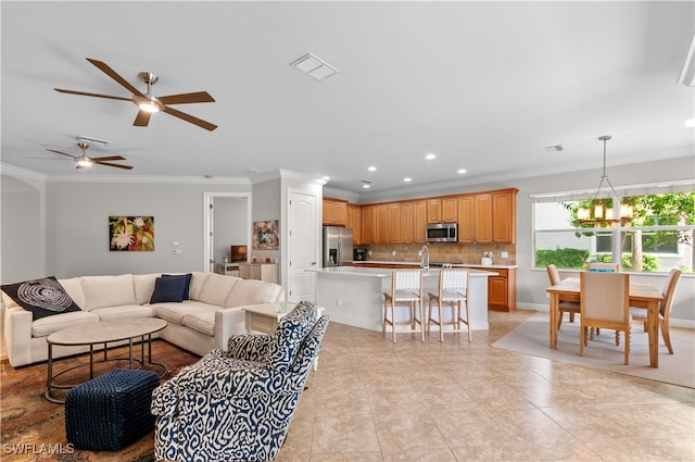 living room with ornamental molding, light tile patterned flooring, sink, and ceiling fan with notable chandelier