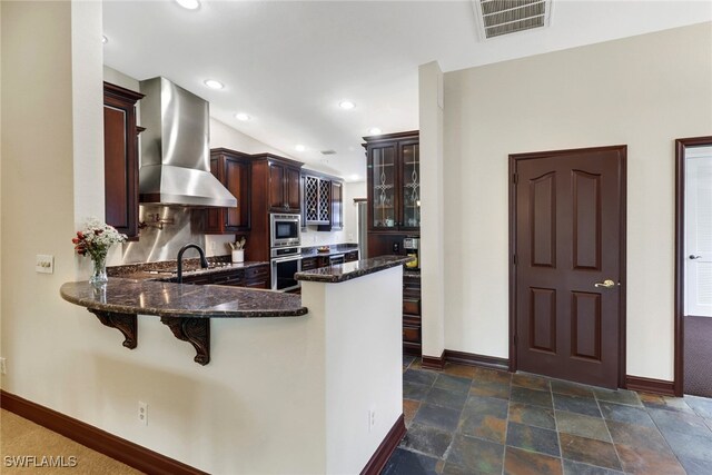 kitchen featuring appliances with stainless steel finishes, range hood, kitchen peninsula, and dark stone counters