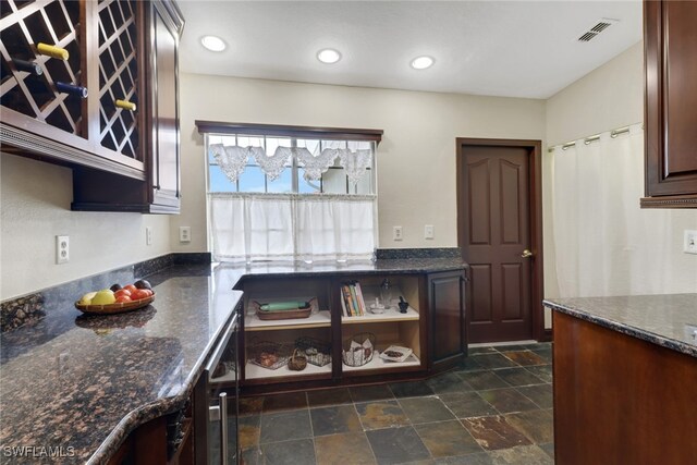 kitchen featuring dark stone countertops, beverage cooler, and dark brown cabinetry