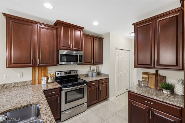 kitchen with light tile patterned floors, appliances with stainless steel finishes, sink, and light stone counters