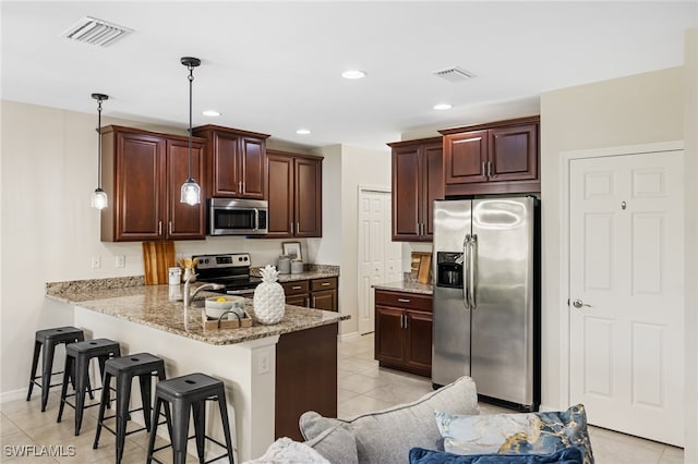 kitchen featuring light tile patterned floors, kitchen peninsula, a breakfast bar area, appliances with stainless steel finishes, and decorative light fixtures