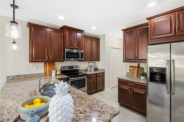 kitchen featuring light tile patterned floors, appliances with stainless steel finishes, hanging light fixtures, and light stone countertops