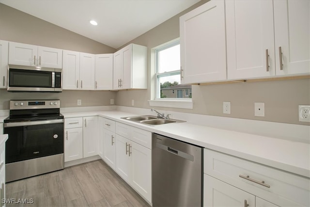 kitchen with appliances with stainless steel finishes, white cabinetry, sink, and vaulted ceiling