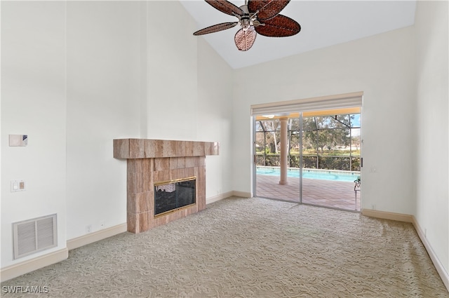 unfurnished living room with high vaulted ceiling, ceiling fan, carpet floors, and a tile fireplace