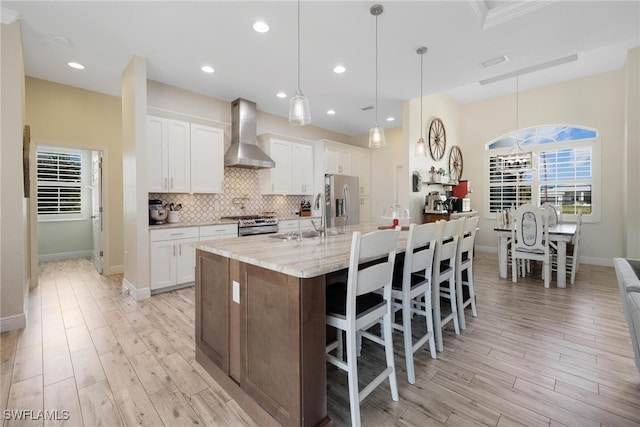 kitchen featuring wall chimney exhaust hood, pendant lighting, white cabinets, and stainless steel appliances