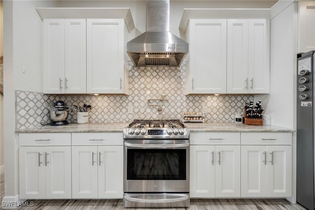 kitchen featuring backsplash, wall chimney exhaust hood, stainless steel range, white cabinets, and light stone counters