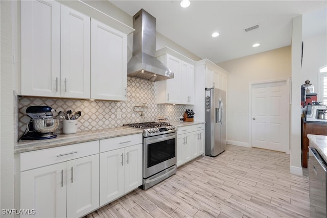 kitchen featuring white cabinets, appliances with stainless steel finishes, light hardwood / wood-style floors, wall chimney exhaust hood, and light stone counters