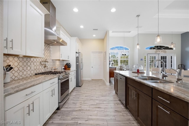 kitchen featuring wall chimney range hood, appliances with stainless steel finishes, white cabinetry, pendant lighting, and sink