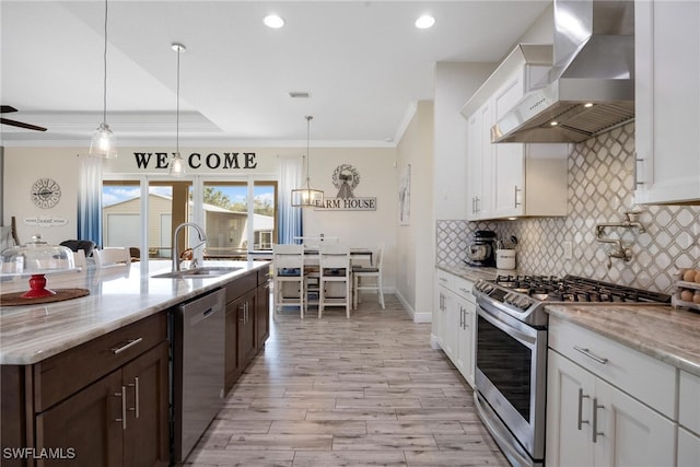 kitchen with wall chimney range hood, stainless steel appliances, sink, light wood-type flooring, and light stone counters