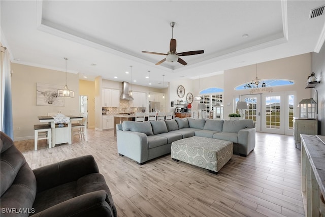 living room featuring light hardwood / wood-style flooring, a tray ceiling, and ceiling fan with notable chandelier