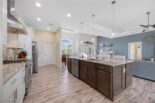 kitchen with wall chimney exhaust hood, sink, white cabinets, decorative light fixtures, and appliances with stainless steel finishes