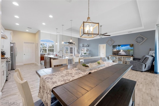 dining space featuring light hardwood / wood-style floors, sink, a tray ceiling, and ceiling fan with notable chandelier