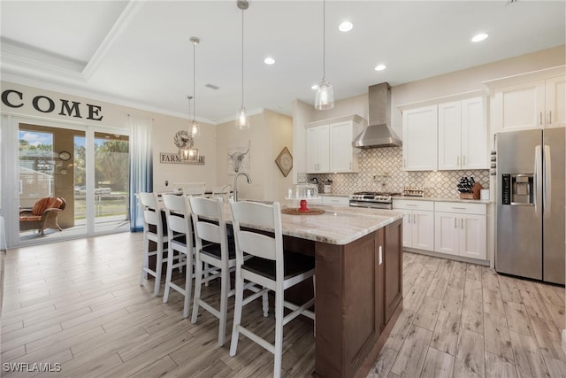 kitchen with white cabinets, stainless steel appliances, wall chimney exhaust hood, and hanging light fixtures