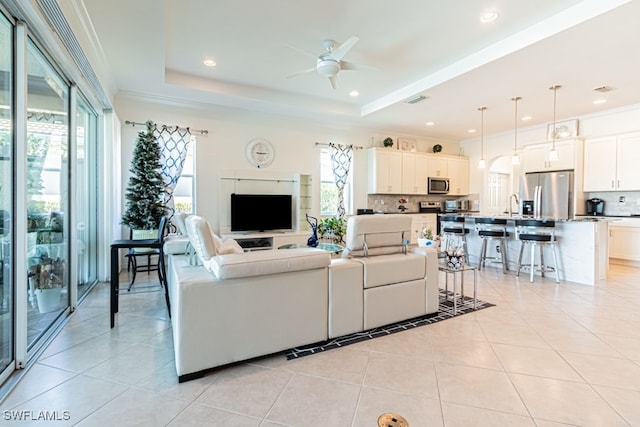 living room with a raised ceiling, light tile patterned floors, plenty of natural light, and ceiling fan