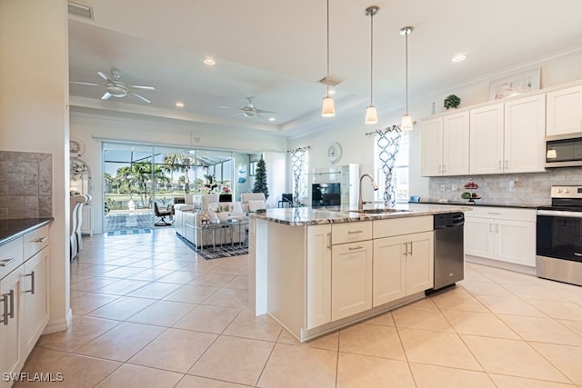 kitchen with light tile patterned floors, a kitchen island with sink, stainless steel appliances, sink, and decorative light fixtures