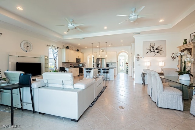 living room featuring light tile patterned flooring, a tray ceiling, and ceiling fan