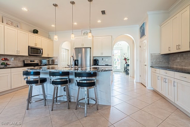 kitchen featuring appliances with stainless steel finishes, crown molding, light tile patterned floors, and an island with sink