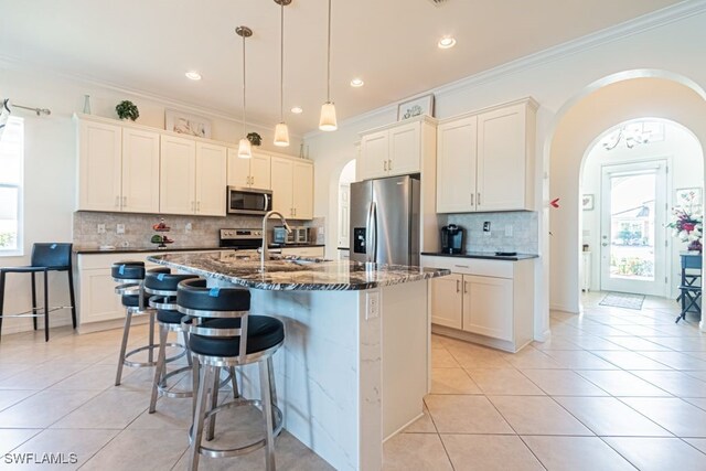 kitchen featuring an island with sink, crown molding, pendant lighting, appliances with stainless steel finishes, and tasteful backsplash