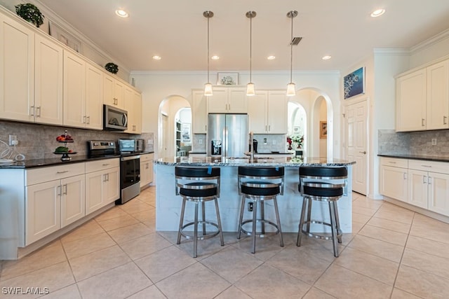 kitchen with appliances with stainless steel finishes, a kitchen island with sink, decorative light fixtures, and backsplash