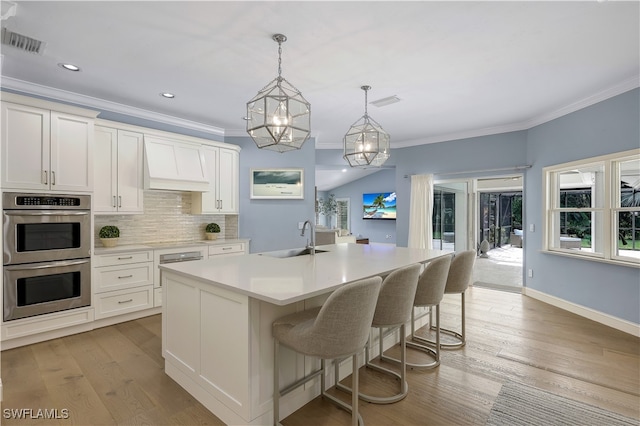 kitchen featuring white cabinets, stainless steel double oven, sink, and an island with sink