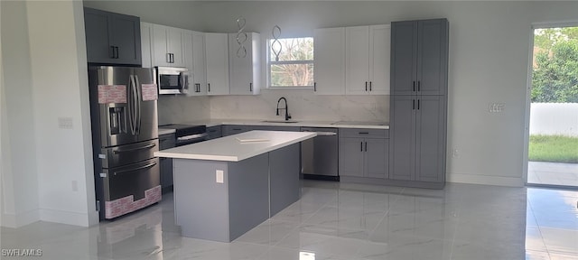 kitchen with gray cabinets, a center island, appliances with stainless steel finishes, and tasteful backsplash