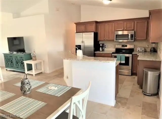 kitchen with lofted ceiling, a center island, appliances with stainless steel finishes, and light stone counters