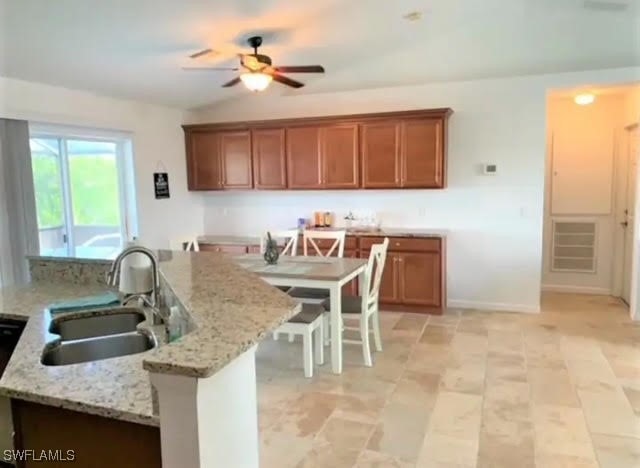 kitchen with light stone countertops, sink, a kitchen bar, and ceiling fan