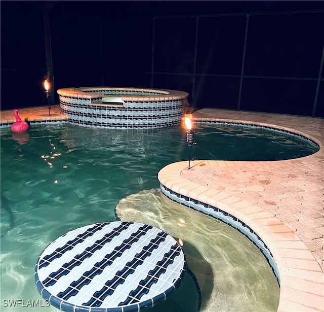 pool at twilight featuring an in ground hot tub