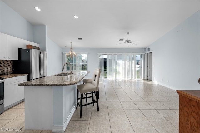 kitchen featuring stainless steel fridge, white cabinetry, hanging light fixtures, and a kitchen island with sink