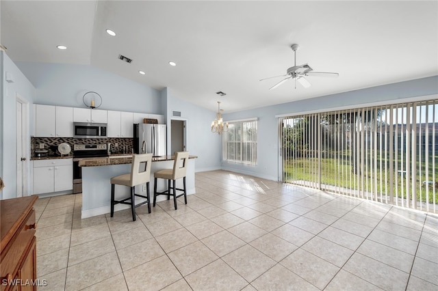 kitchen featuring a healthy amount of sunlight, appliances with stainless steel finishes, a kitchen breakfast bar, lofted ceiling, and white cabinets