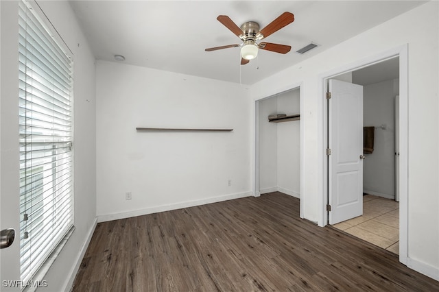 unfurnished bedroom with multiple windows, a closet, dark wood-type flooring, and ceiling fan