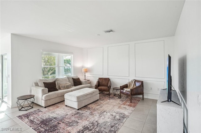 living area featuring light tile patterned floors, visible vents, and a decorative wall