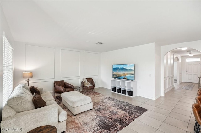 living room featuring light tile patterned floors, visible vents, arched walkways, and a decorative wall